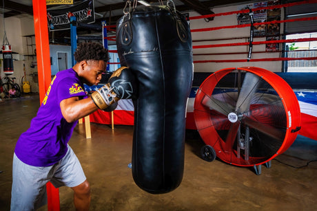 Boxer practices on the punching bag with a red Maxx Air drum fan cooling him near the ring.