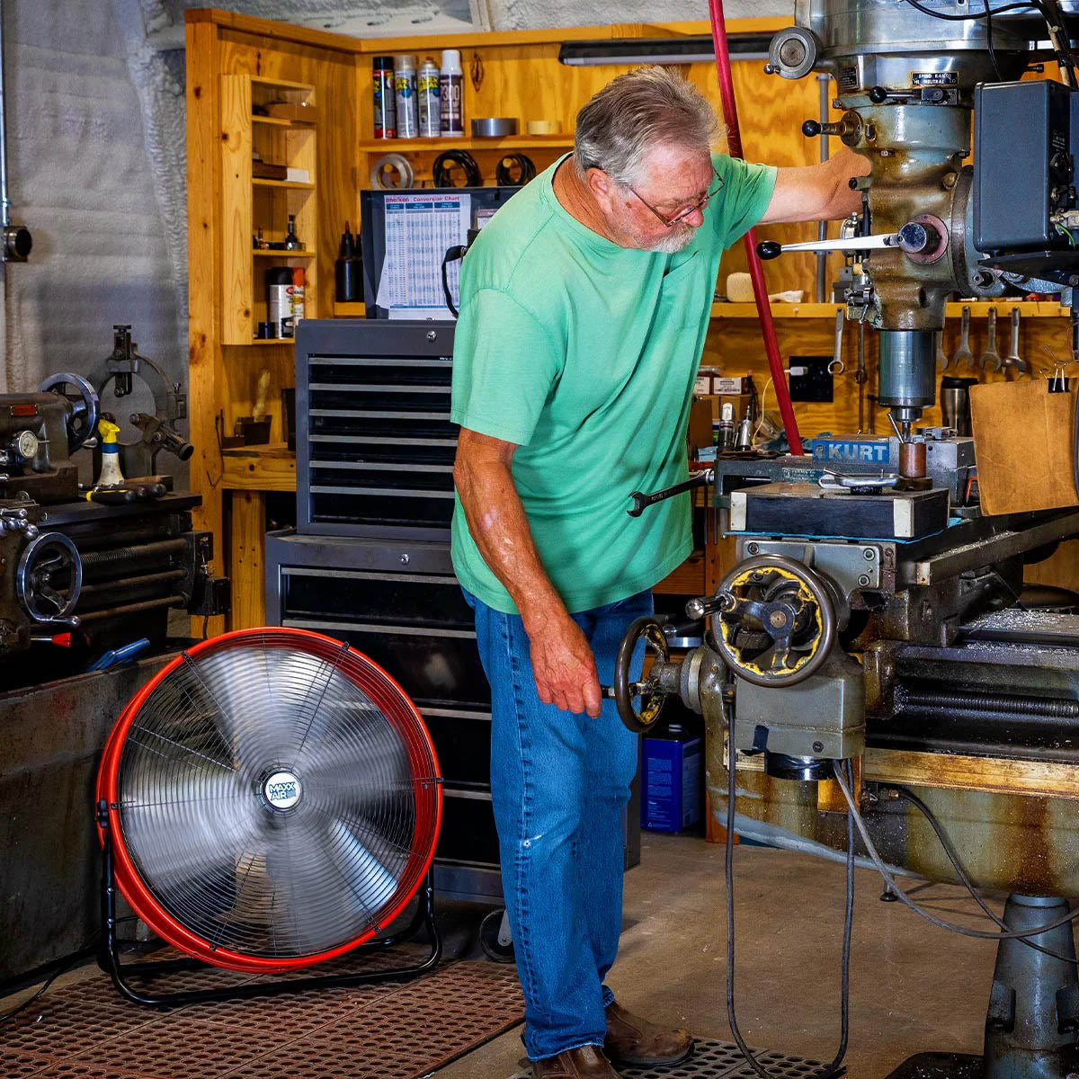 Employee in a factory works on machinery with the 24" tilt fan cooling him in the background.