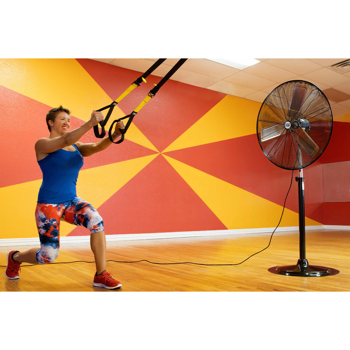 Commercial pedestal fan unit cooling an athlete in a large room during a gym workout.