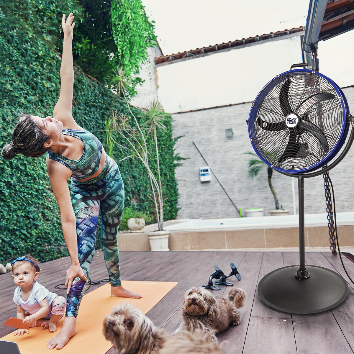 The 20 in. stand fan used outdoors on a home patio while a woman practices yoga around her child and pets.