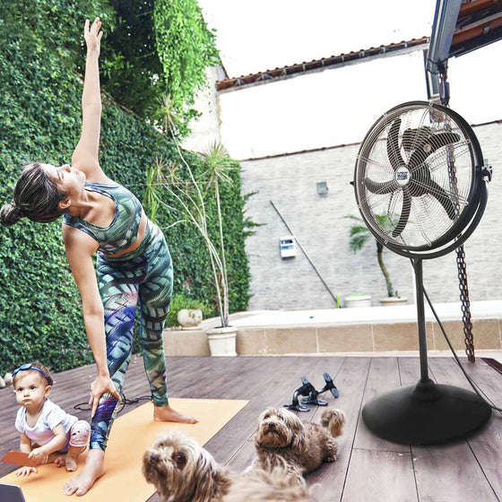 The 20 in. stand fan used outdoors on a home patio while a woman practices yoga around her child and pets.